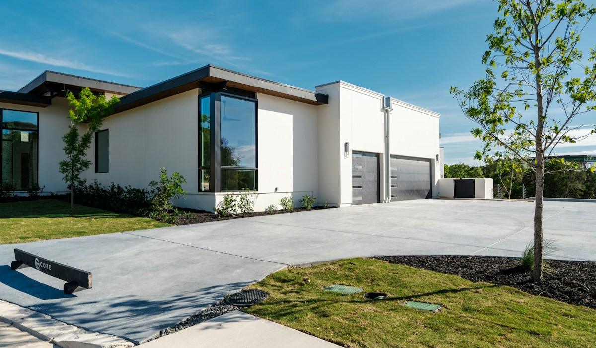 Modern white house with large windows fronted by a wide, freshly finished concrete driveway