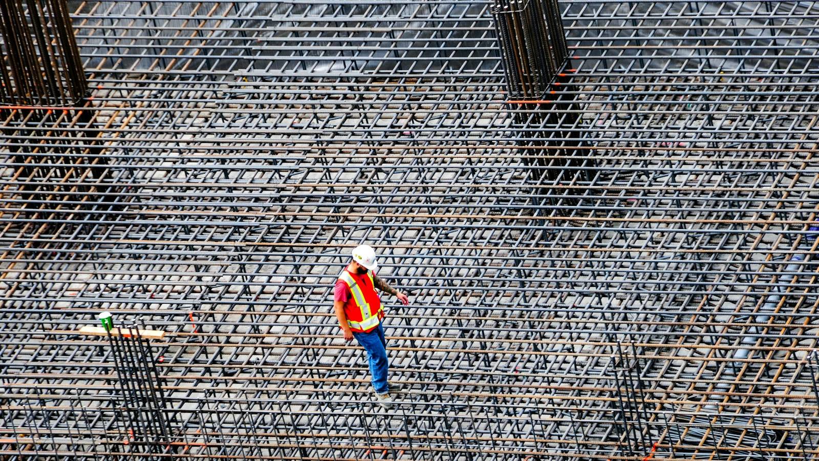 Construction worker inspecting a tied rebar grid laid out over a prepared building foundation